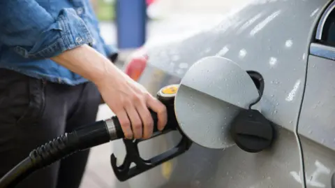 Getty Images A woman holds a gas pump as she fills up her car